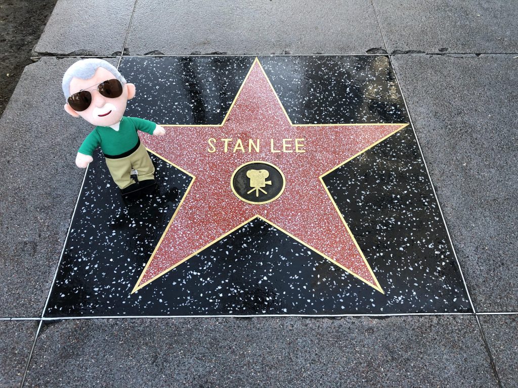 Stan Lees star on the Hollywood Walk of Fame along with a small plush doll of Stan Lee in a green sweater and khaki pants.