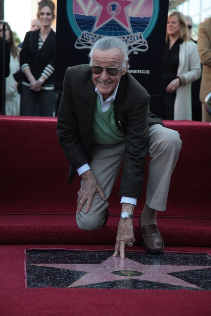 Stan Lee kneeling down in front of his star on the Hollywood Walk of Fame.