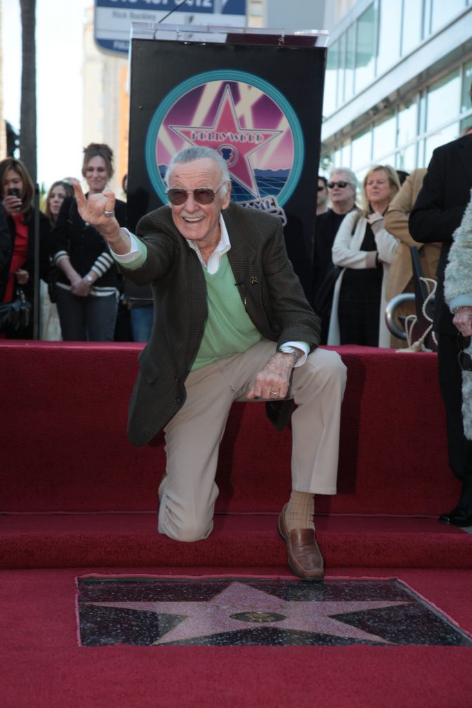 Stan Lee kneeling in front of his star on the Hollywood Walk of Fame.