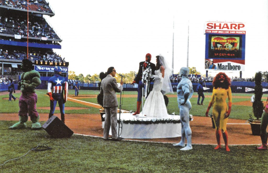 Stan Lee officiating Spider-Man and Mary Jane's wedding on the field of Shea Stadium surrounded by people dressed as Hulk, Captain America, Iceman and Firestar