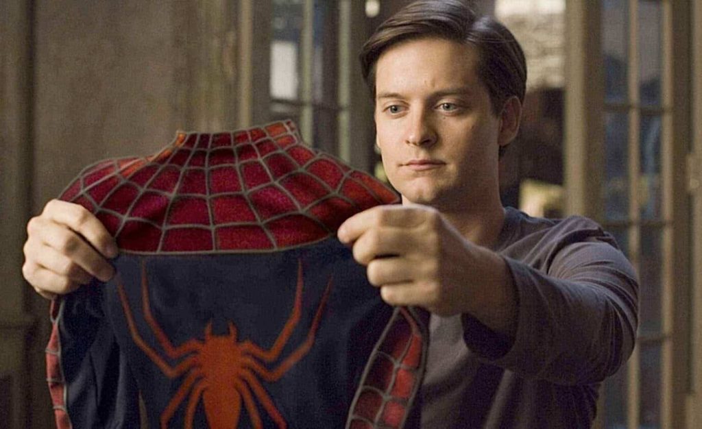 Tobey Maguire holds up a red and blue Spider-Man costume