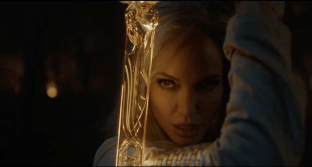 A close up of Angelina Jolie in Marvel's The Eternals, holding a gold sword in front of her face