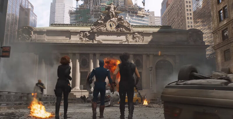 Black Widow, Captain America, and Hawkeye in costume run towards Grand Central Terminal in New York as chaos ensues around them.