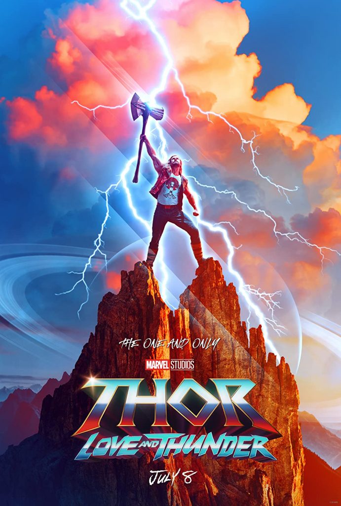 A blue sky with yellow, orange and red clouds in the background and Thor in jeans, a white t-shirt and jacket holding his ax, Stormbreaker, atop two mountain peaks.