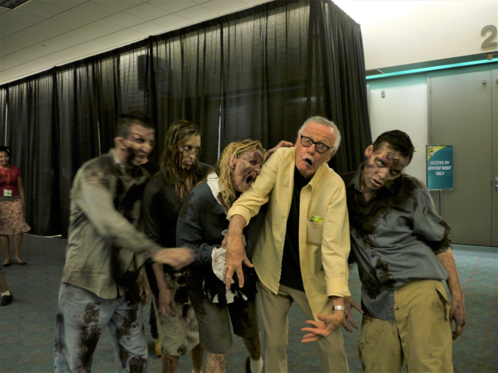 Stan Lee poses as a zombie with a group of The Walking Dead cosplayers in the hall at San Diego Comic Con